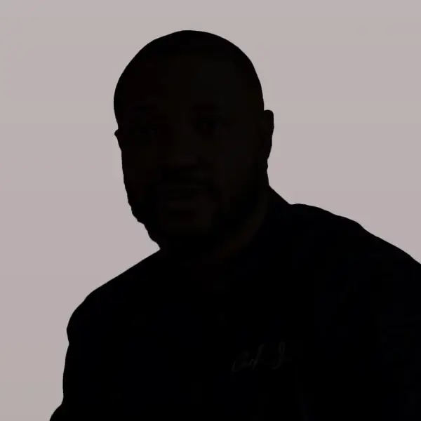 A man with short hair and a beard, featured in an Alcohol Recovery Mindset Coaching Case Study, sits against a plain, light background. His features are hard to distinguish due to the dim lighting.